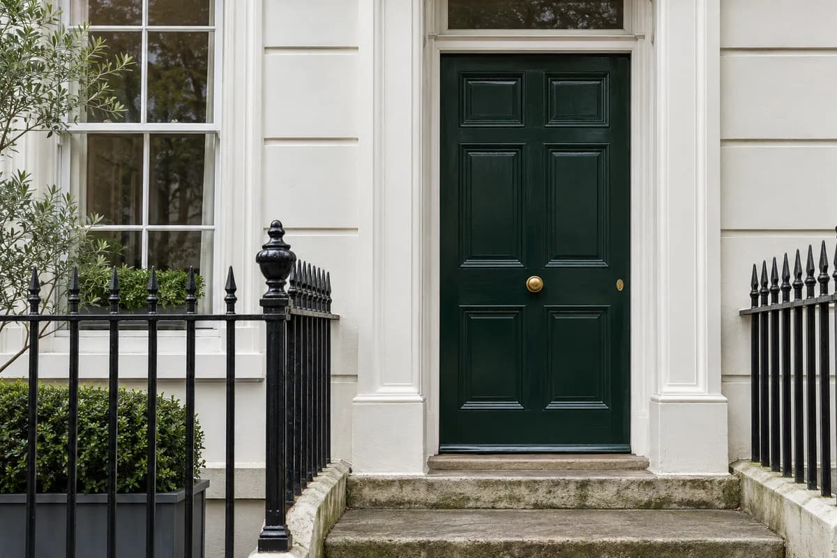 Illustrative green panelled front door, white stucco and black railings